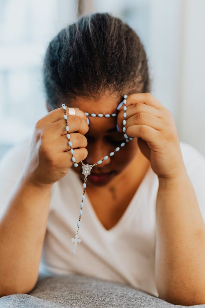 a woman in white shirt praying while holding a rosary